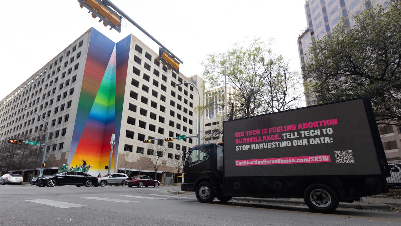 Image of a billboard truck in front of a city block in Austin, Texas. The billboard truck reads, "Big tech is fueling abortion surveillance. Tell tech to stop harvesting our data"