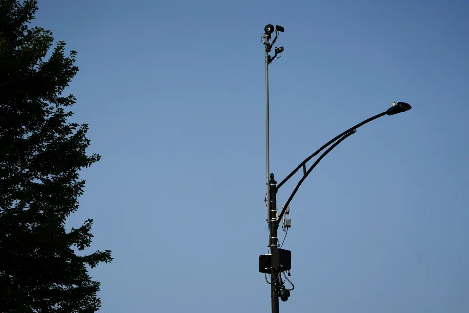 An image of a lightpole silhouetted against a blue sky. A few electronic devices are attached.